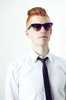Giving the look of a suit a new spin. A red haired male standing in a suit and sunglasses with a white background.