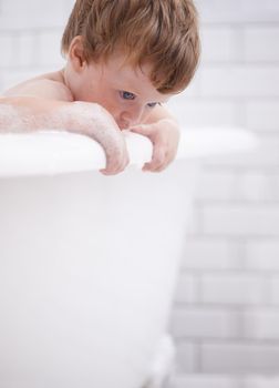 Getting fresh and clean. Tiny red-headed toddler in the bath tub.