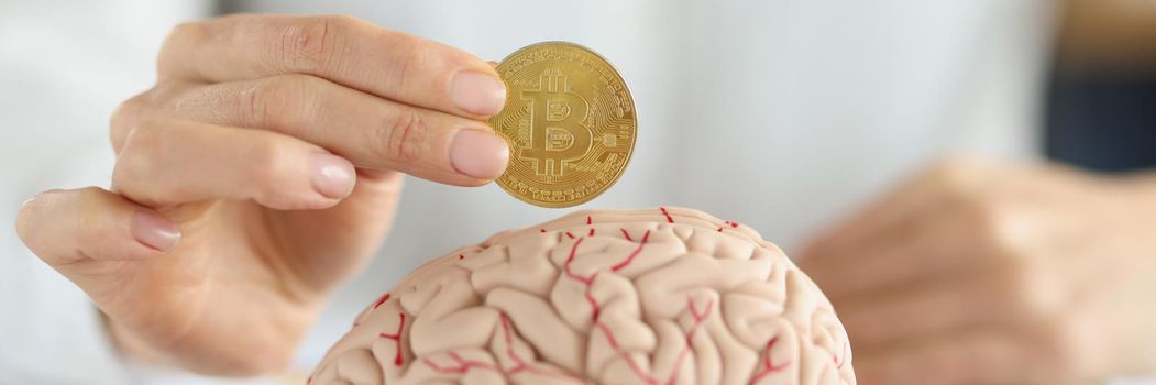 Businesswoman holding bitcoin coin in front of human brain