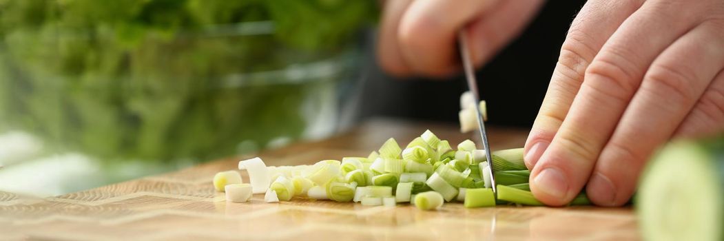Professional chef cut spring onion with sharp knife on cutting board