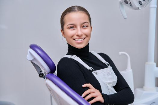 Portrait of young smiling teenage girl in dental chair looking at camera