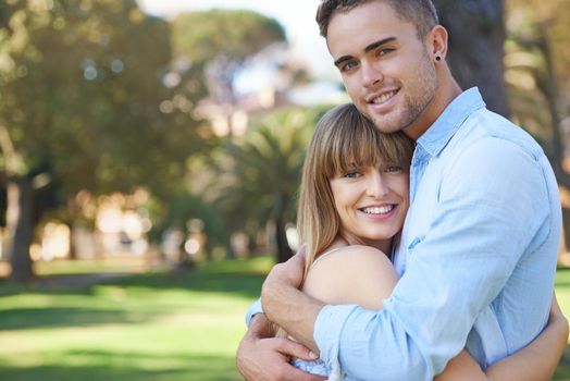 Sweet young love. Portrait of a young couple embracing while standing in a park.