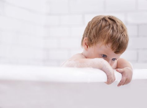 Getting fresh and clean. Tiny red-headed toddler in the bath tub.