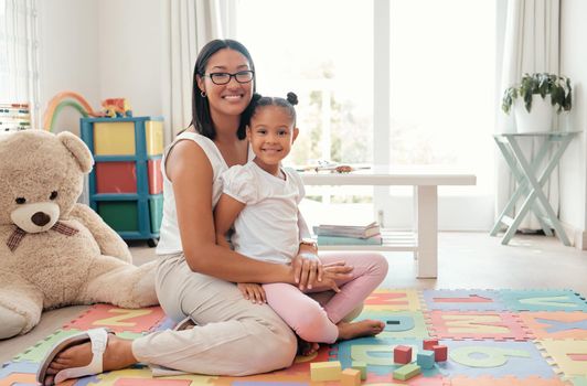 Portrait of a happy mother and child in a playroom playing with education building blocks. Happiness, care and smile of woman holding and sitting with her girl kid in colorful room with toys at home.