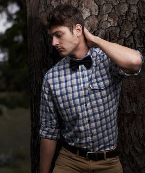 Hipster outing. a young man in a shirt and bowtie standing in front of a tree.