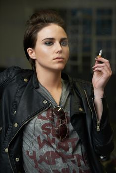Attitude and attractive. a rebellious looking young woman smoking a cigarette in a car garage.