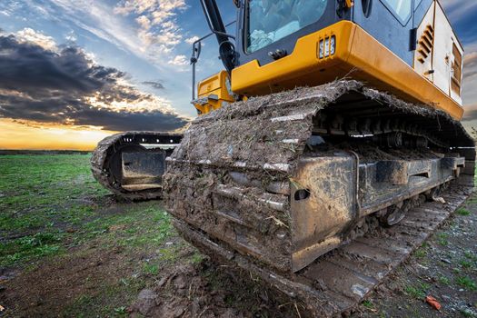 Crawler excavator during earthmoving works on construction site at sunset