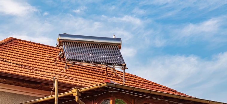 Solar water heater installed on tile roof of house for eco heating of water. Large water tank. Horizontal photo.