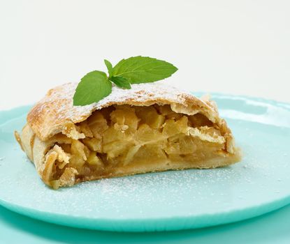 Slice of apple strudel on a round plate, white background