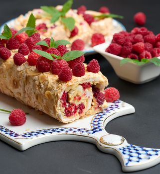 Baked meringue roll with cream and fresh red raspberry on a black wooden board