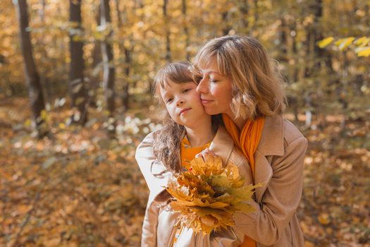 Young mother with her little daughter in an autumn park. Fall season, parenting and children concept.