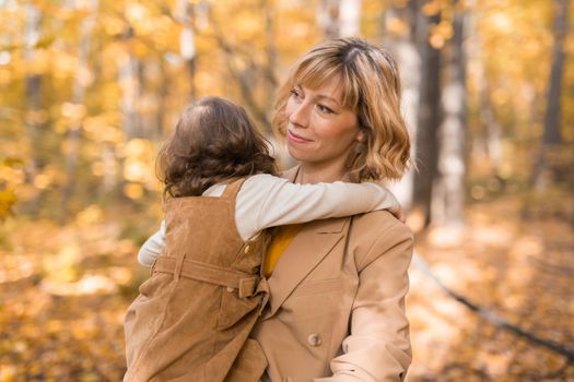 Mother with child in her arms against background of autumn nature. Family and season concept.