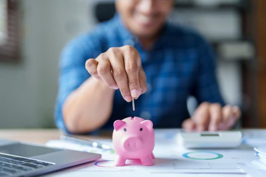 Portrait of an Asian businessman using a calculator to calculate his savings from SME operations, with a pink piggy bank as keep money concept