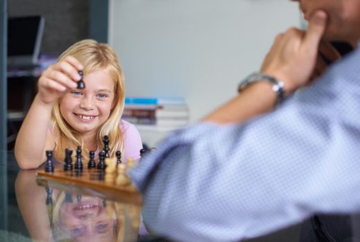 Teaching her the skill of strategy. A father playing chess with his young daughter.