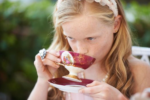 Sipping her tea like a lady. A cute little girl having a tea party outside.