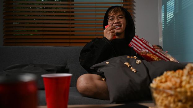 Man enjoy eating popcorn and watching movie at home. Entertainment and leisure activity concept