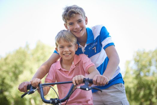 Teaching him all he knows about riding. Portrait of two brothers sitting on a bicycle while playing outside.