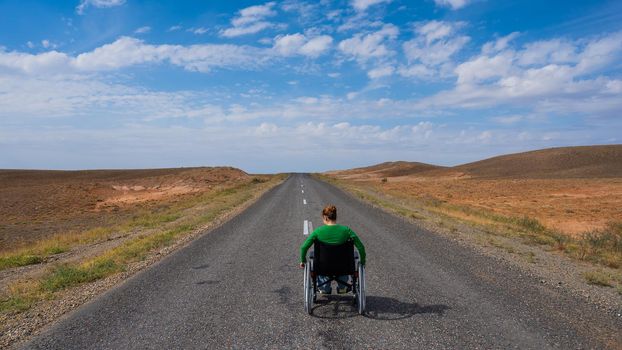 Woman in a wheelchair on a highway in the steppes.