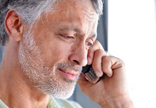 A friendly phone conversation. A mature man looking down and smiling while having a phone conversation.