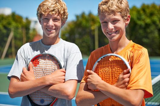 Tennis is their sport of choice. Two friends standing together and holding their tennis rackets on the court.