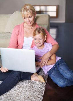 In touch with family online. a mother and daughter sitting on their living room floor and using a laptop