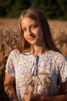 Portrait of beautiful smiling girl holding some rye ears sitting on the ground in the field of ripe wheat