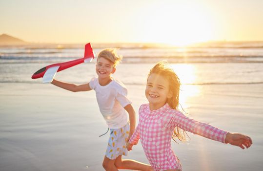 Children running with airplane toys on beach together for wellness, exercise and healthy development on sunset horizon and ocean waves. Kids having fun and playing for outdoor summer holiday portrait