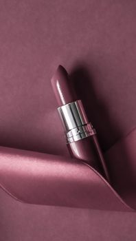 Luxury lipstick and silk ribbon on purple holiday background, make-up and cosmetics flatlay for beauty brand product design