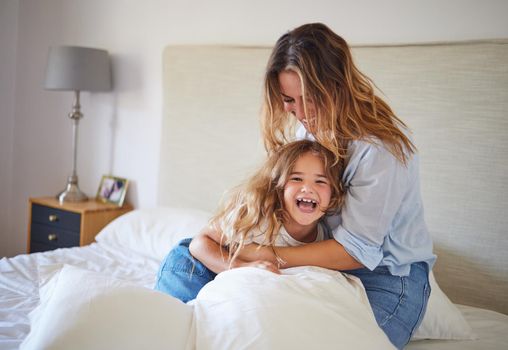 Mom and child on the bed playing together, having fun and laughing. Portrait of mother and daughter in bedroom, smiling while woman tickle young girl. Family, love and laughter in morning at home