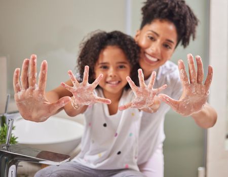 A mom teaching child to clean their hands, using soap and water in the bathroom to destroy germs to stay healthy. Kid washing dirty hand, keeps family health safe and prevent dangerous bacteria