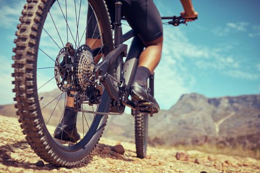 Bicycle, sport and wheels on a dirt road adventure trail on a mountain for fitness and exercise. Closeup of a bike, track and an athlete turning the tire in sand while cycling in nature for fun.