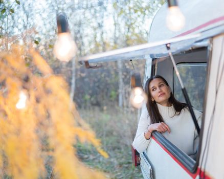 Portrait of a caucasian woman looking out of a trailer window. Travel in a camper in autumn.