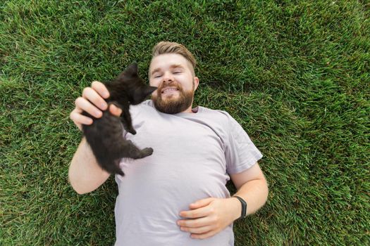 Man with little kitten lying and playing on grass - friendship love animals and pet owner concept