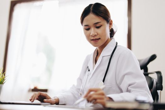 Portrait of an Asian female doctor using a computer and tablet to work