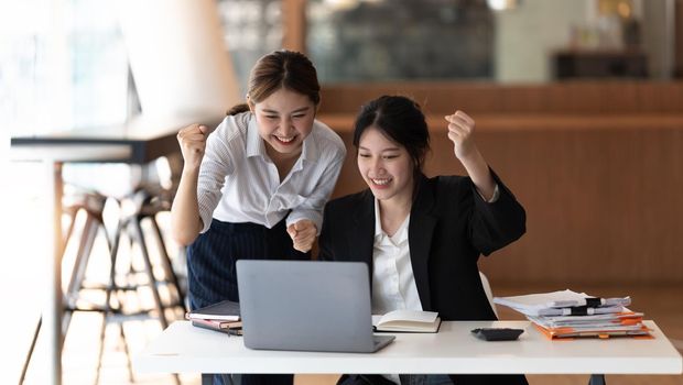 Two asian woman excited business team celebrate corporate victory together in office