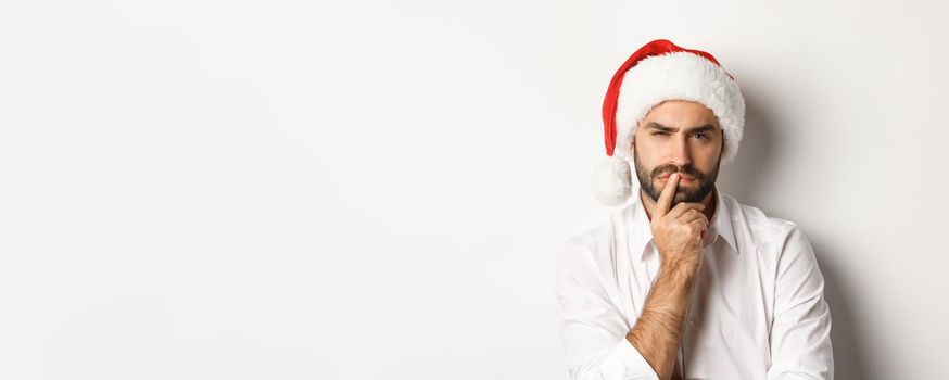 Party, winter holidays and celebration concept. Serious man thinking about christmas and new year, wearing santa hat, white background