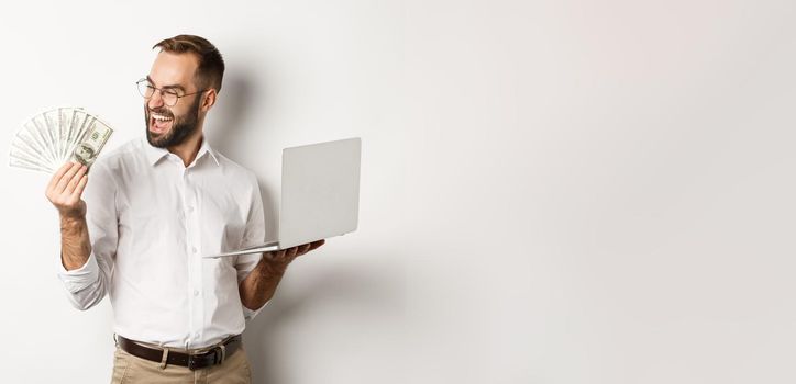 Business and e-commerce. Successful businessman using laptop for work and holding money, standing over white background