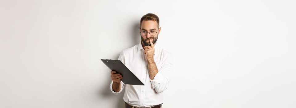 Thoughtful employee looking at clipboard, having doubts, standing over white background