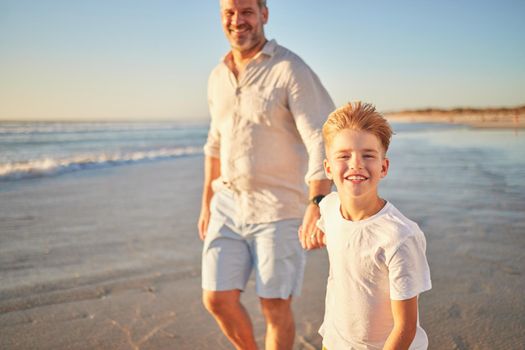 Father and son bonding on a beach, walking alone the ocean and holding hands at sunset. Portrait of an excited child enjoying and ocean trip and peaceful walk with a loving, caring parent in nature