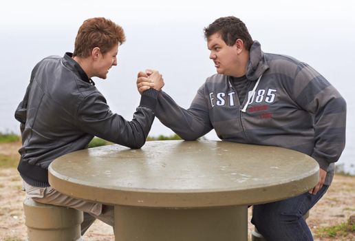 You havent got a chance. Two friends having an arm wrestling competition outside.