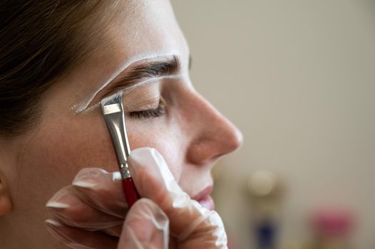 The master draws the shape of the eyebrows with white paint before coloring.