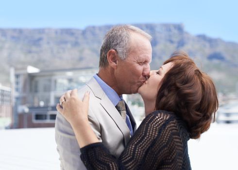 Kissing against a scenic backdrop. A mature couple kissing one another against a scenic background.