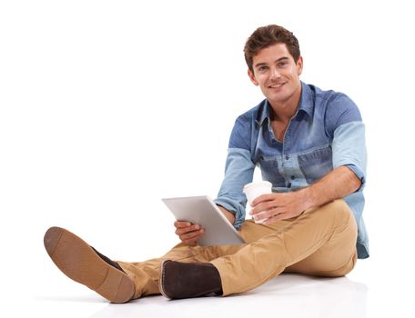 Browsing the internet in his free time. A casual young man sitting against white with his digital tablet.