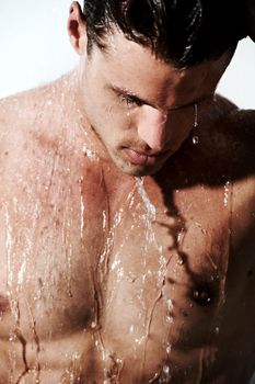 Taking a shower. A muscular young man under the running water of a shower.