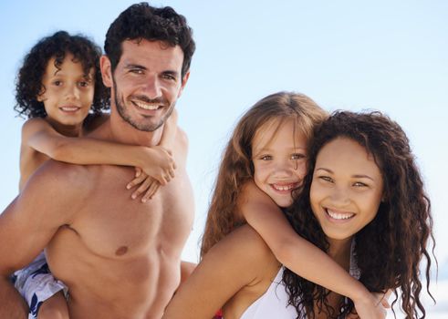 Getting away from it all. A family of four in swimwear smiling against a bright sky.
