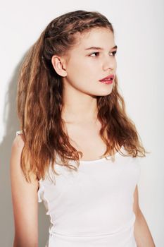 Looking casual. A pretty young teenage girl standing against a white background.