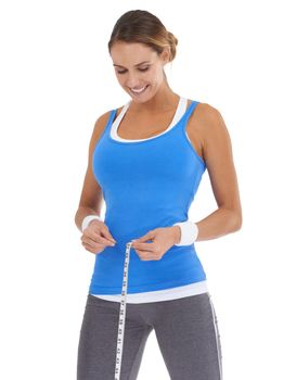 Ive lost inches already. Young woman in sportswear measuring her waistline while isolated on white.