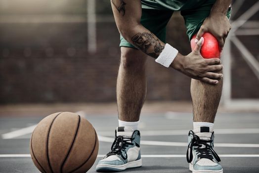 Sports, injury in basketball and knee pain or athlete man while on an outdoors court holding his hurt leg during training or exercise for hobby. Closeup of male hands on glowing red body part