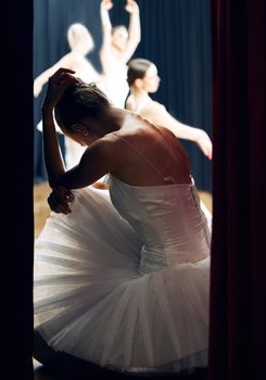 Dancer thinking backstage at ballet concert or recital while group on theater stage. Girl ballerina waiting on floor of auditorium, anxiety and nerves, for performance in front of audience or crowd