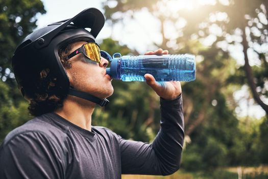 Cyclist, water and bottle in forest for hydration, with cycling equipment and sunglasses by trees for wellness. Man, drink and sports while exercise, workout or training for fitness outside in woods